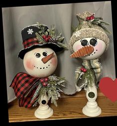 two snowmen with hats and scarfs on top of a wooden table next to a red heart