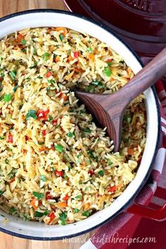 a bowl filled with rice and vegetables next to a wooden spoon