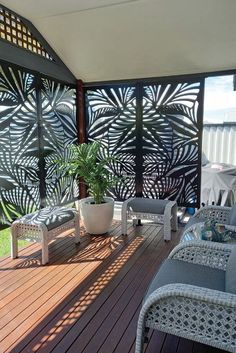 a deck with chairs and a potted plant on top of it, next to a privacy wall