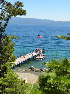 a boat is docked at the end of a pier with people sitting on it and an american flag flying in the background