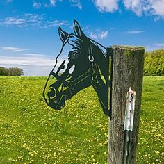 a horse head cut out of the side of a wooden post in a field with dandelions