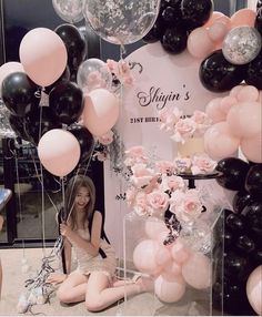 a woman sitting on the ground with balloons and flowers in front of her at a birthday party