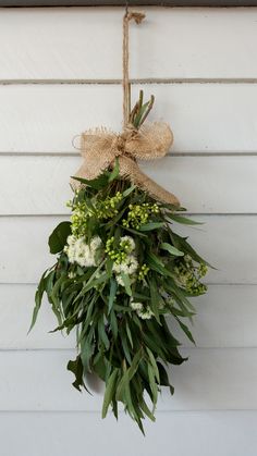 a wreath hanging on the side of a white house with greenery and burlap