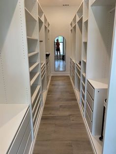 an empty walk - in closet with white shelving and drawers on both sides, while a person is reflected in the mirror