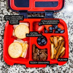 an open red lunch box filled with fruit and crackers on top of a marble counter