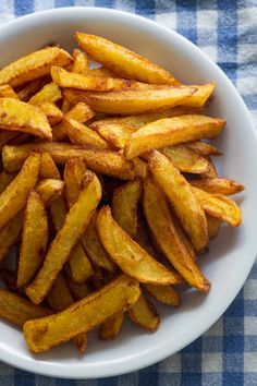 a white bowl filled with french fries on top of a blue and white checkered table cloth