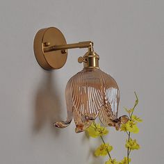 a wall mounted light that is next to a vase with flowers in it and yellow flowers on the side