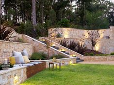 an outdoor living area with stone walls and seating on the grass, surrounded by trees