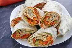 a white plate topped with lots of veggies wrapped in tortilla wrap