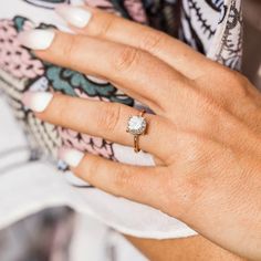 a woman's hand with a diamond ring on her left hand and a flower print shirt on the right