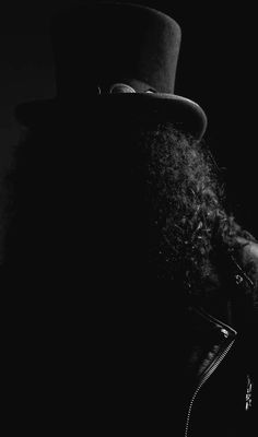 a black and white photo of a man with long hair wearing a top hat in the dark