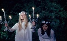 two girls dressed in white holding candles and looking at the camera while standing next to each other