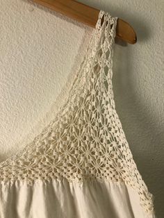 a white crochet top hanging on a wooden hanger next to a wall