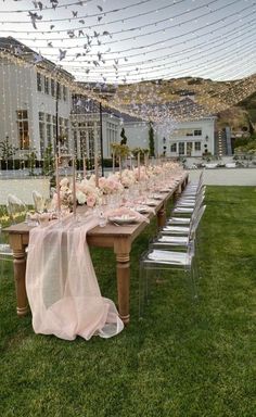 a long table is set up with pink and white flowers on it, surrounded by clear chairs