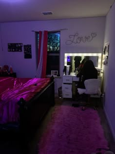 a person sitting at a desk in front of a bed with a pink blanket on it