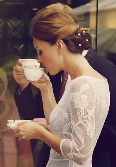 a woman in a white dress drinking out of a cup