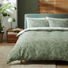 a bed with green comforter and pillows in a room next to a plant on the floor