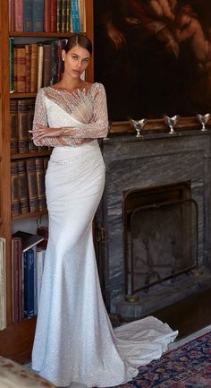 a woman standing in front of a book shelf wearing a long sleeved wedding dress