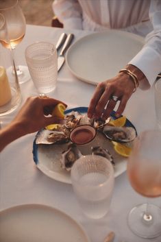 two people are serving oysters on a plate at a table with wine glasses and silverware