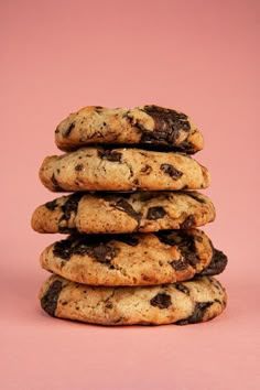 a stack of chocolate chip cookies against a pink background with the top one half eaten