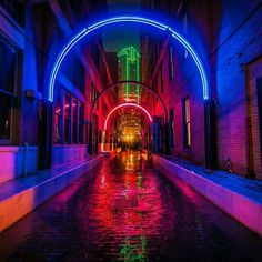 an alley way with neon lights on the buildings and water running under it at night