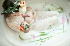 a baby is laying in a bowl with flowers on it's head and body