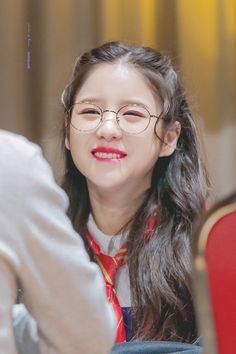 a woman wearing glasses sitting in front of a red chair