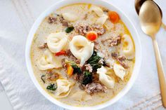 a bowl of soup with dumplings, meat and carrots on a white table cloth