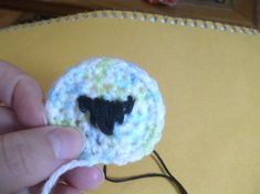 a hand holding a small crocheted sheep brooch with black face on it