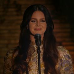 a woman with long hair standing in front of a microphone and smiling at the camera