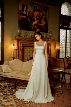 a woman in a white wedding dress standing next to a couch