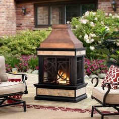 an outdoor fireplace in the middle of a patio with chairs around it and flowers on either side