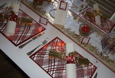 red and gold place settings on a white table with silverware, napkins and candles