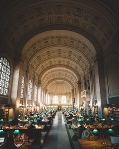 the inside of a large library with many tables and lamps on each side of the room