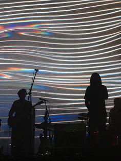 two people standing in front of a large screen with light streaks on the wall behind them