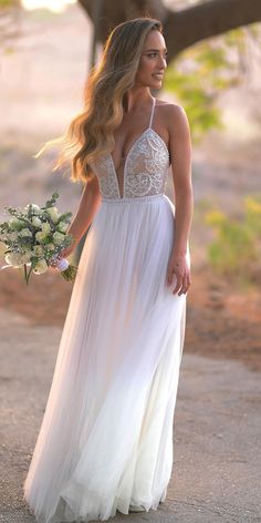 a woman in a white dress is walking down the road holding a bouquet and looking off into the distance