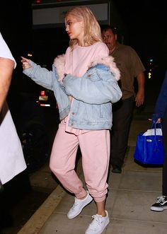 a woman in pink sweatpants and denim jacket walking down the street with her hand on her hip