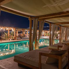 an outdoor swimming pool at night next to a covered patio with lounge chairs and tables