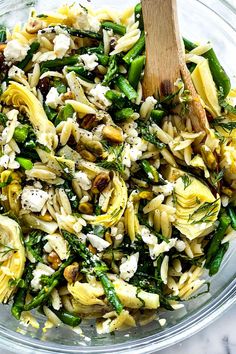 a glass bowl filled with pasta salad and a wooden serving spoon in it's side dish