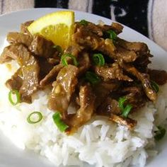 a white plate topped with rice and meat covered in gravy next to a slice of lemon