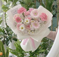 a woman holding a bouquet of pink and white flowers in front of a planter