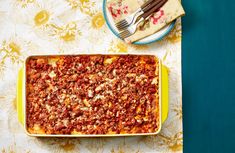 a casserole dish with meat and cheese in it next to a fork on a floral tablecloth