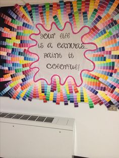 an art project is displayed on the wall above a computer screen with words written in rainbow colors