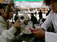 two people sitting at a table taking pictures with their cell phones