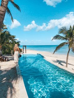 a woman sitting on the edge of a swimming pool next to palm trees and water