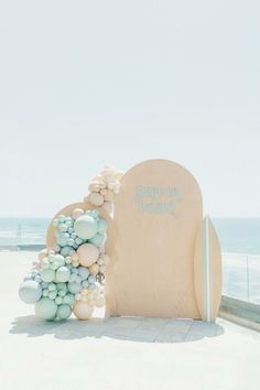 a wooden chair with balloons attached to it near the beach and ocean in the background