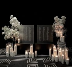 several tall vases filled with white flowers and lit candles on a black table cloth