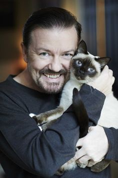 a man holding a cat in his arms and looking at the camera with a smile on his face