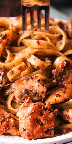 a plate full of pasta with chicken and sauce on it, being held by a fork