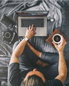 a man sitting on a bed with his laptop and cup of coffee in front of him